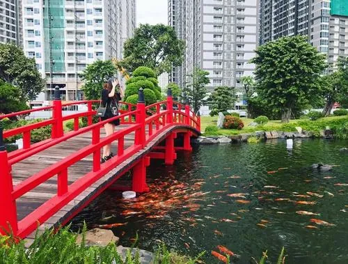 ảnh công viên Tân Cảng cầu đi bộ màu đỏ nổi bật bắc qua hồ nước, người dạo bước chậm rãi, cây xanh hai bên tạo khung cảnh hài hòa và rất dễ chịu