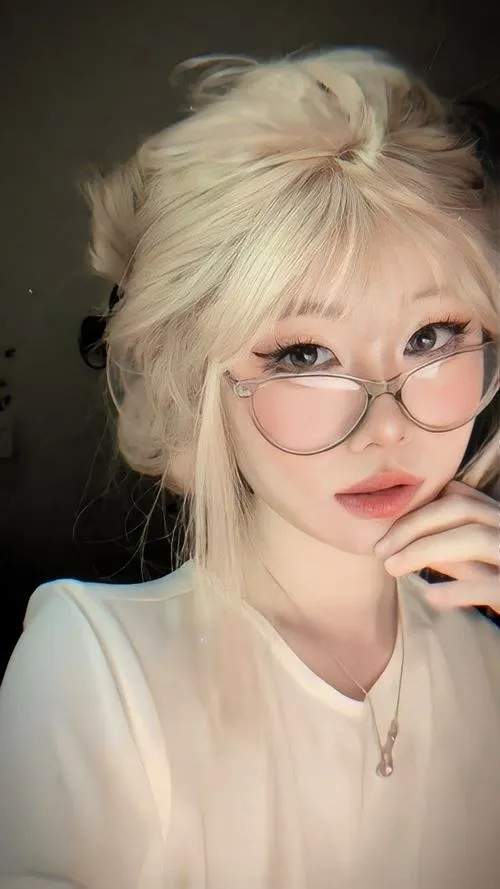 Gái xinh tóc vàng hoe đeo kính tròn khẽ đỡ cằm nhìn thẳng máy với nụ cười nhẹ nhàng toát lên nét đẹp trong sáng.
