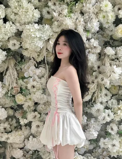 Gái đẹp đứng giữa vườn hoa trắng rực rỡ trong váy dài thanh thoát, nụ cười nhẹ nhàng toát lên vẻ trong sáng.