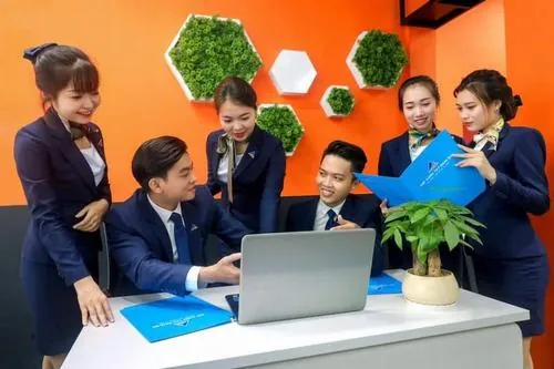 Visual công sở nổi bật của nhóm chuyên viên đang trao đổi tài liệu quanh bàn làm việc, sắc cam xanh từ hồ sơ và đồng phục làm khung hình thêm sinh động