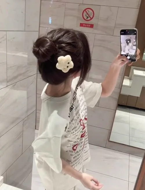 Hình ảnh mỹ nhân che mặt mặc áo thun basic quần legging yoga đứng trước tường bê tông cầm điện thoại.