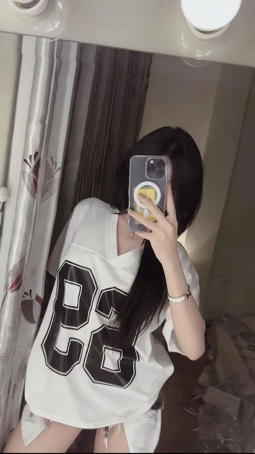 Ảnh selfie ẩn danh mặc set đồ tất cả đen tóc búi thấp đứng trong studio ánh sáng neon cầm điện thoại.