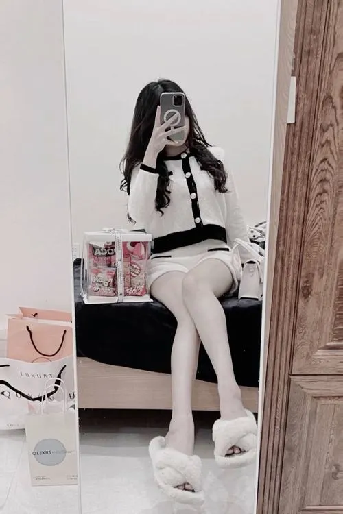 Gái xinh mặc áo sơ mi kẻ caro quần cargo ngồi trên xe máy cầm điện thoại che mặt.