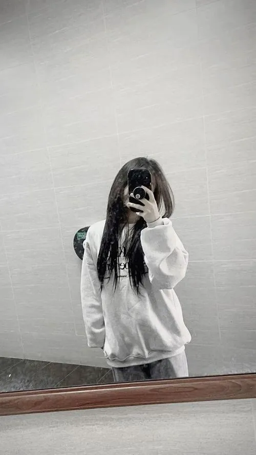 Thiếu nữ mặc crop top ren trắng quần jeans rách đứng trên cầu thang cầm điện thoại giấu mặt.