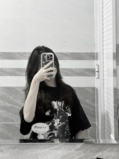 Gái xinh mặc đầm bodycon đỏ rượu vang tóc xoăn lớn đứng trong club ánh sáng mờ cầm điện thoại.