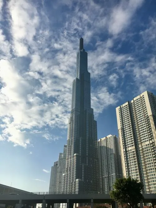 Khung hình tập trung vào phần chân tháp với dòng người qua lại, làm nổi bật sự tương phản giữa công trình và nhịp sống