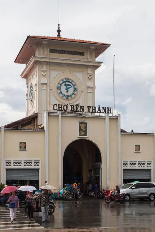 Một góc cận cảnh cổng chính với bảng hiệu rõ ràng, người bán hàng đứng gần lối vào, không khí buôn bán nhẹ nhàng của điểm đến du khách quốc tế hiện lên chân thật