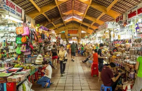 ảnh khu chợ trung tâm bên trong với lối đi đầy màu sắc từ gian hàng vải, ánh đèn vàng chiếu xuống tạo cảm giác ấm áp và nhộn nhịp đặc trưng của hồn cốt đô thị