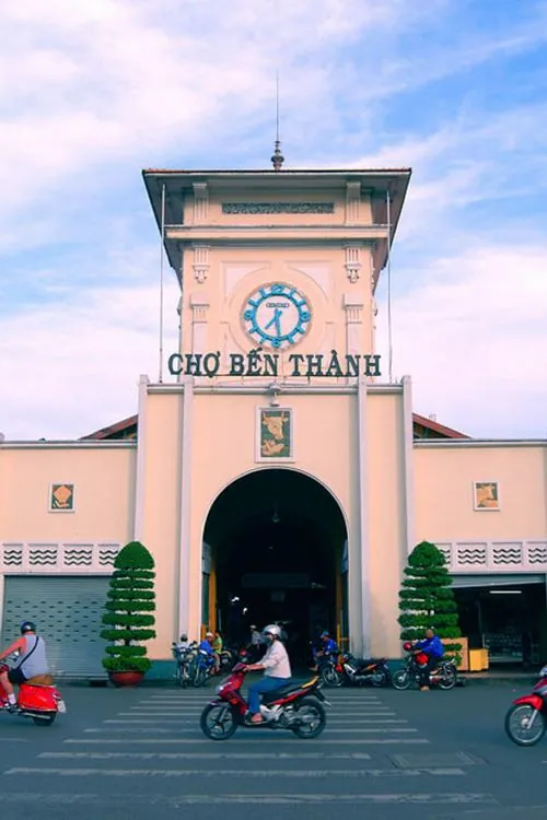 ảnh ngôi chợ trăm tuổi chụp cổng chính với bầu trời xanh trong, vài cụ già ngồi nghỉ bên lề đường, tạo nên nét chậm rãi hiếm thấy giữa trung tâm đông đúc