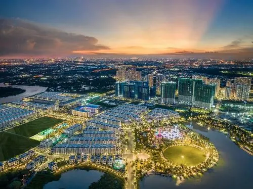 Ảnh dự án góc hoàng hôn nhìn toàn khu đô thị với ánh đèn bắt đầu lên, mặt nước phản chiếu sắc cam nhẹ tạo nên khung cảnh vừa hiện đại vừa ấm áp của Vinhomes Grand Park