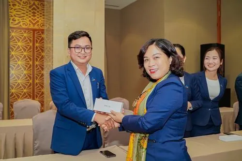 Ảnh trai xinh gái đẹp ghi lại ba nhân sự đứng cạnh sofa phòng khách văn phòng, vest xanh chỉn chu và dáng đứng thoải mái tạo cảm giác thân thiện chuyên nghiệp