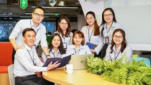 Nhóm nữ nhân viên quây quần bên nhau trong văn phòng, nụ cười tự nhiên cùng đồng phục sáng màu tạo cảm giác gần gũi và duyên dáng