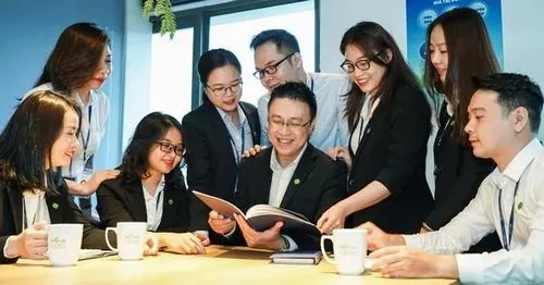 Nhóm nhân viên ngồi họp quanh bàn làm việc với laptop và tài liệu mở sẵn, ai cũng tập trung trao đổi trong không gian văn phòng giao dịch chuyên nghiệp