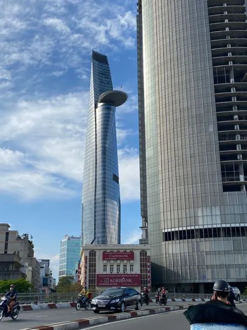 Khung cảnh buổi trưa nắng gắt làm lớp kính phản chiếu mạnh, khiến toàn bộ tòa nhà sáng rực và nổi bật giữa nền trời