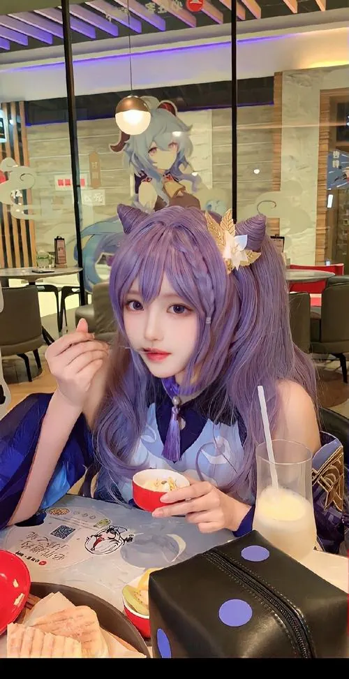 Ảnh cosplay keqing khi người mẫu tóc tím ngồi bên bàn ăn, ánh mắt nhìn thẳng tạo cảm giác gần gũi và dễ thương.