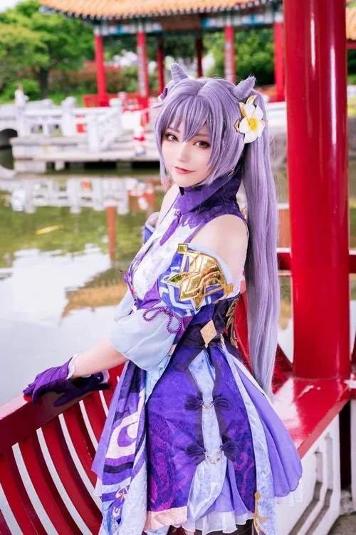 Cosplayer tóc tím tạo dáng ngoài trời với trang phục Liyue, ánh sáng tự nhiên làm rõ phần vai áo và phụ kiện vàng.