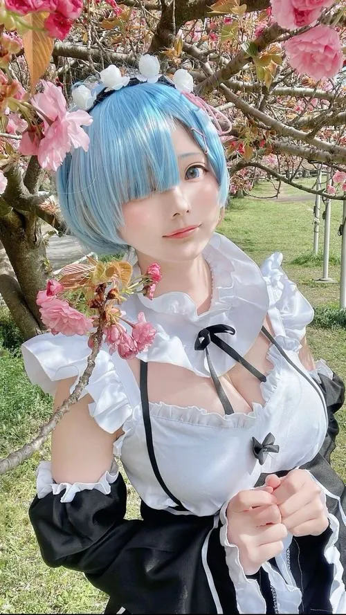 Cosplayer tóc xanh đứng giữa vườn hoa, tay ôm bó hồng trước ngực, gương mặt thanh tú toát nét ngây thơ khó cưỡng.