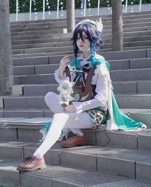 Cosplayer ngồi trên bậc thang trong tạo hình Venti, hạc cầm đặt trên tay và áo choàng xanh trải nhẹ bên chân