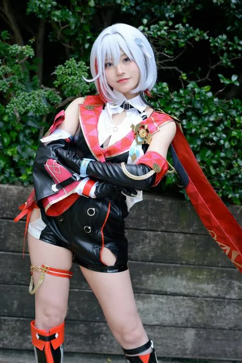 Ảnh Cosplay Honkai Star Rail chụp cosplayer tóc trắng trong bộ đồ đỏ đen, đứng ngoài vườn với ánh sáng tự nhiên.