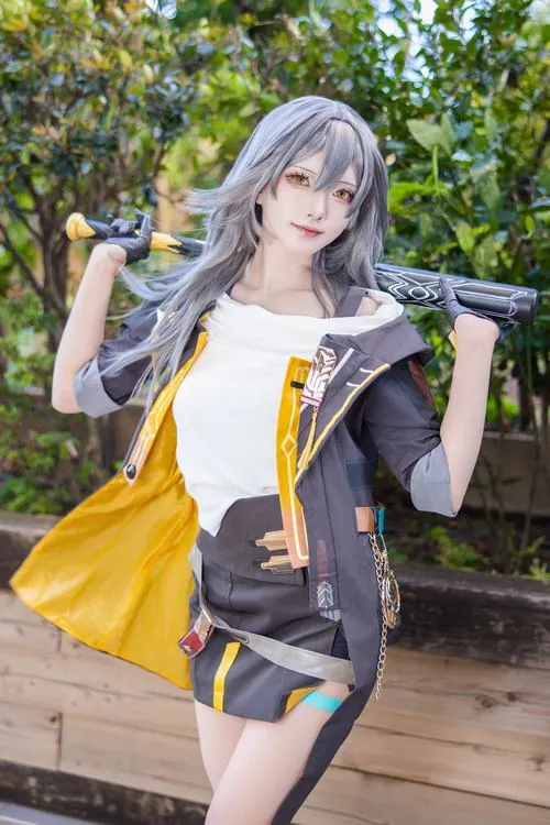 Cosplayer tóc xám mặc trang phục vàng đen đứng ngoài trời, dáng pose tự nhiên giúp bộ ảnh gần gũi hơn.