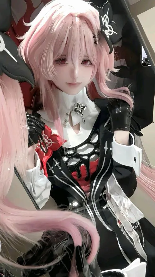 Cosplayer tóc hồng trong trang phục đen đỏ tạo dáng cận mặt, phụ kiện hoa đỏ nổi bật trên nền áo trắng.