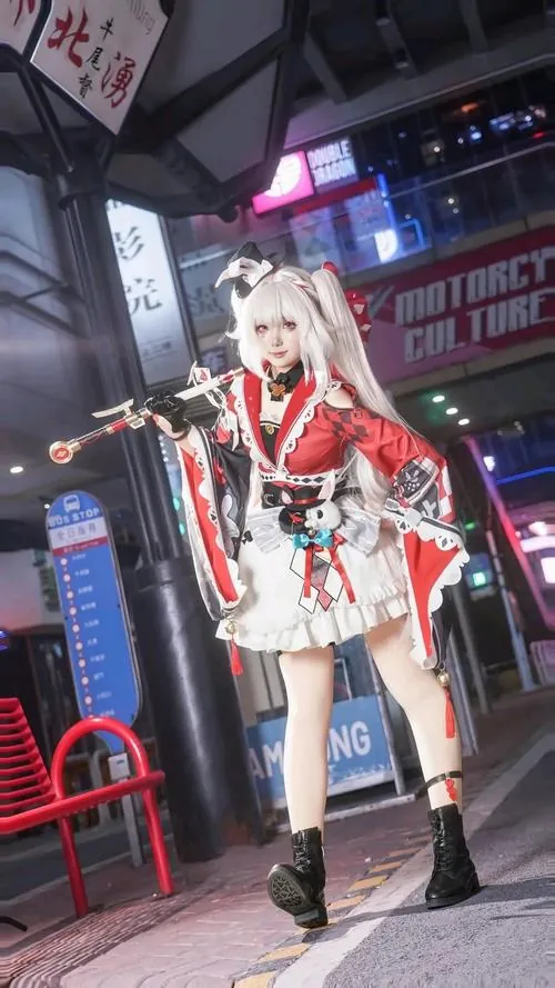 Nữ cosplayer tóc trắng đứng dưới ánh đèn đô thị, bộ đồ trắng đỏ tạo cảm giác năng động giữa khung cảnh đêm.