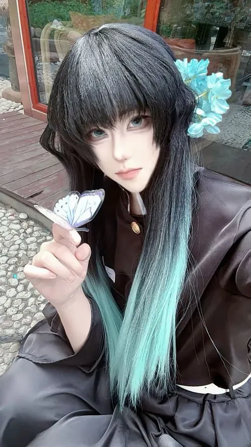 Nữ cosplayer cầm chuôi kiếm gần gương mặt, mái tóc đen pha xanh ngọc rơi mềm trên áo choàng xám trong khung ảnh lạnh